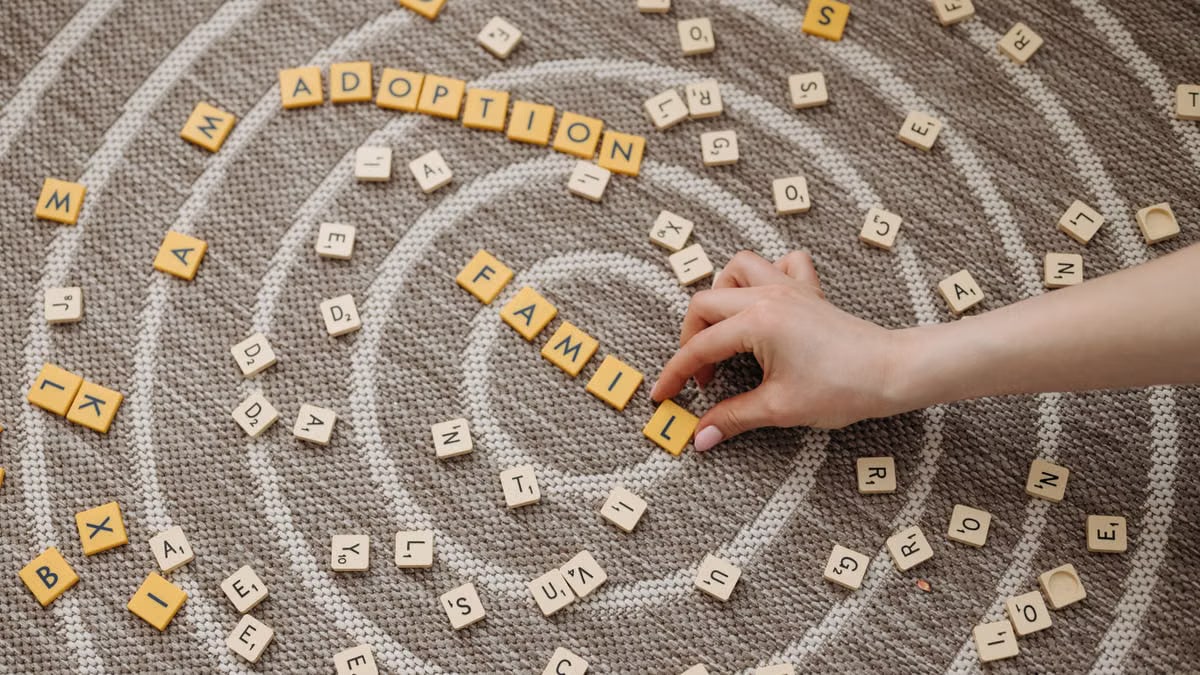A hand arranges letter tiles spelling 'family' and 'adoption' on a circular patterned carpet.